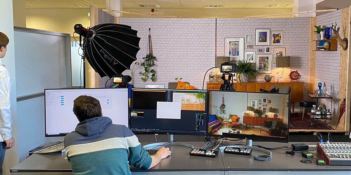 Regieplatz mit Monitoren und Bildmischer vor dem Set, Kameras und Licht im Hintergrund