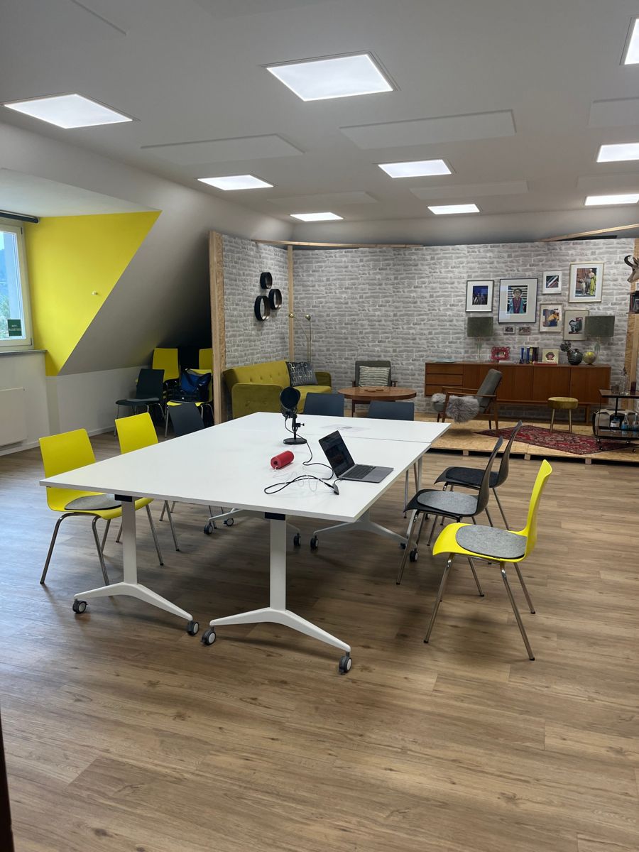 Workshop-Tisch mit Mikrofon und Laptop, dahinter das Wohnzimmer-Set
